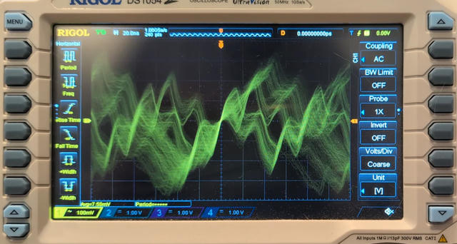 Photo of Rigol DS1054Z oscilloscope in trigger mode with many traces superimposed. The axis scales are 100 mV/division vertically and 20 ns/division horizontally. The signal is nearly 7 divisions tall (700 mV), and the period is 4 divisions horizontally (80 ns) but the waveform is filled with wiggles finer than 1 period long.